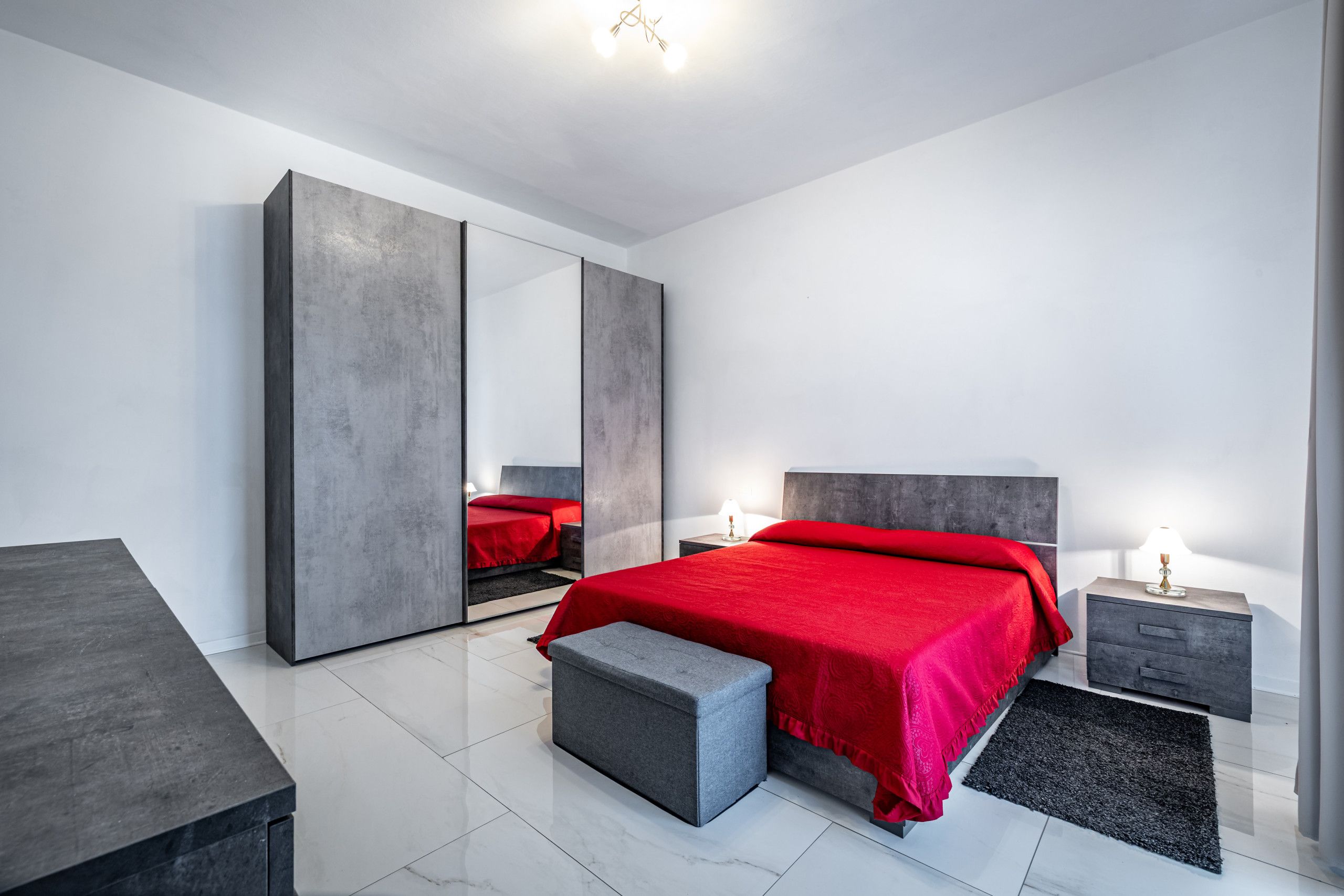 A modern bedroom with a large bed, a wardrobe, a nightstand, and a bench.