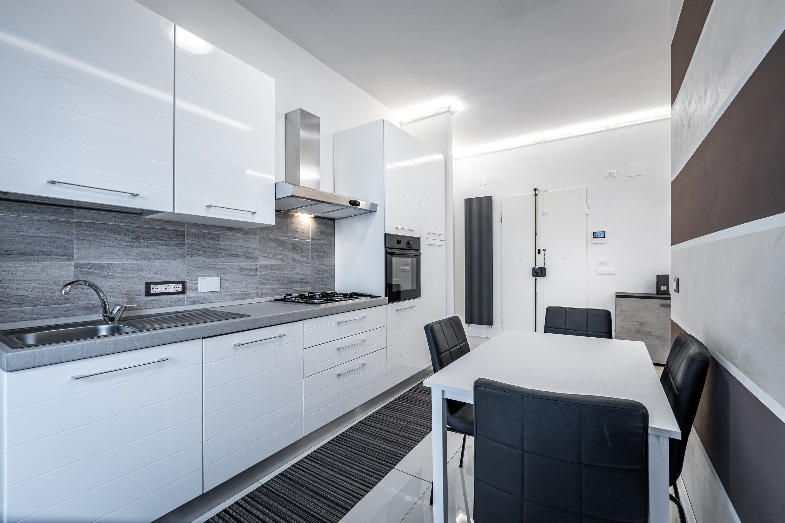 Una cocina moderna con armarios blancos, un lavamanos de acero inoxidable y una estufa integrada.