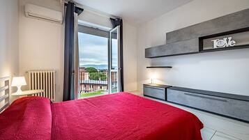 Un cuarto de hotel con una cama, una mesita de noche, una lámpara, un radiador y vistas al exterior.