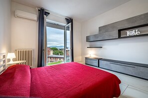 Un cuarto de hotel con una cama, una mesita de noche, una lámpara, un radiador y vistas al exterior.