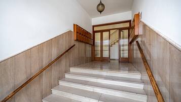 Una escalera con barandillas de madera y piso de mármol que conduce a una puerta con panel de vidrio.