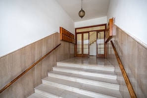 Una escalera con barandillas de madera y piso de mármol que conduce a una puerta con panel de vidrio.