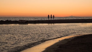 A beach scene with a sunset, calm sea, and a rocky shoreline.