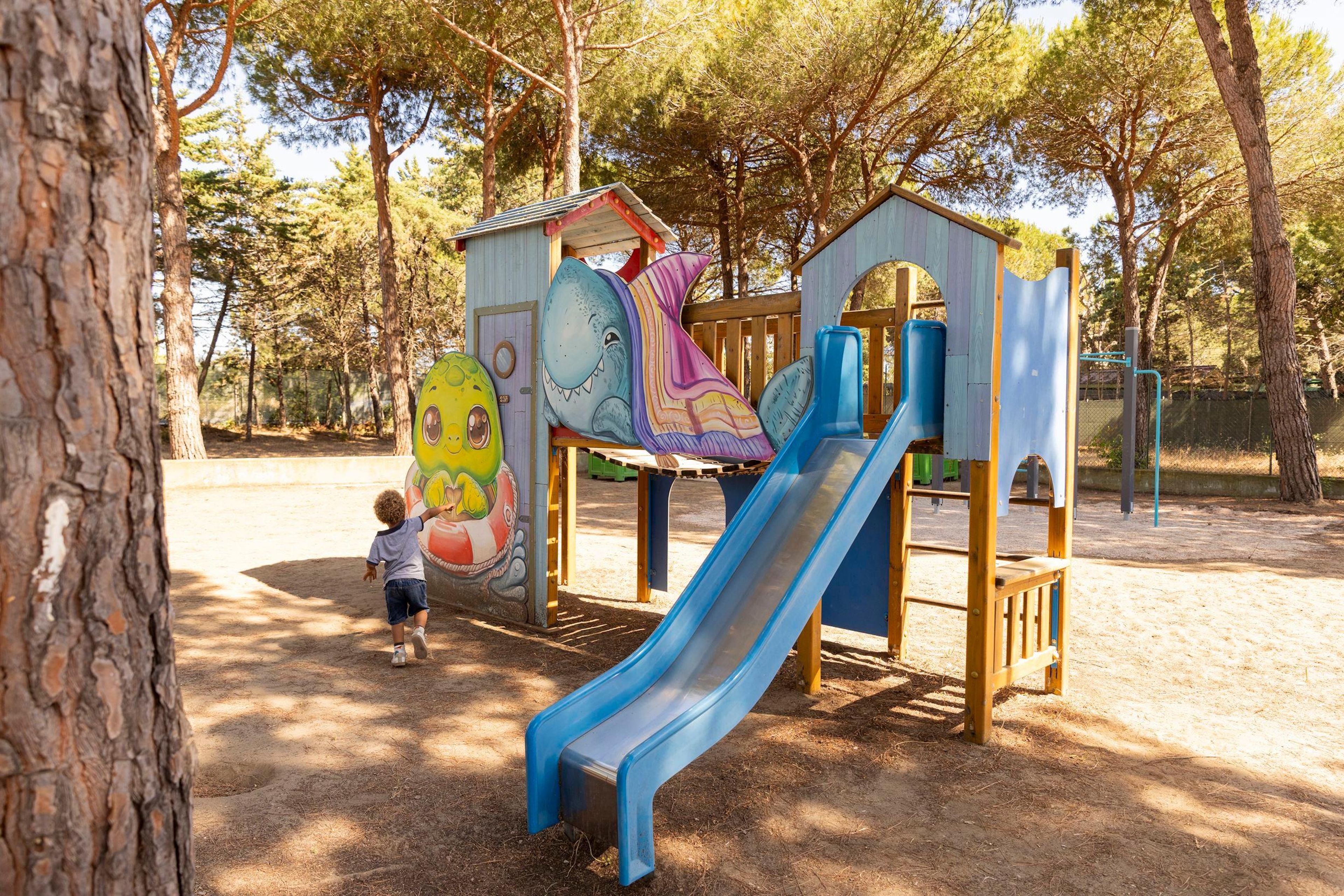 Une aire de jeux avec un toboggan, des structures d’escalade et une fresque murale représentant un requin et un dinosaure.
