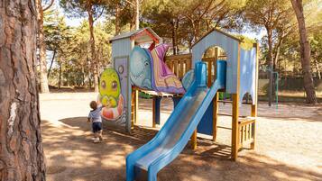 Une aire de jeux avec un toboggan, des structures d’escalade et une fresque murale représentant un requin et un dinosaure.