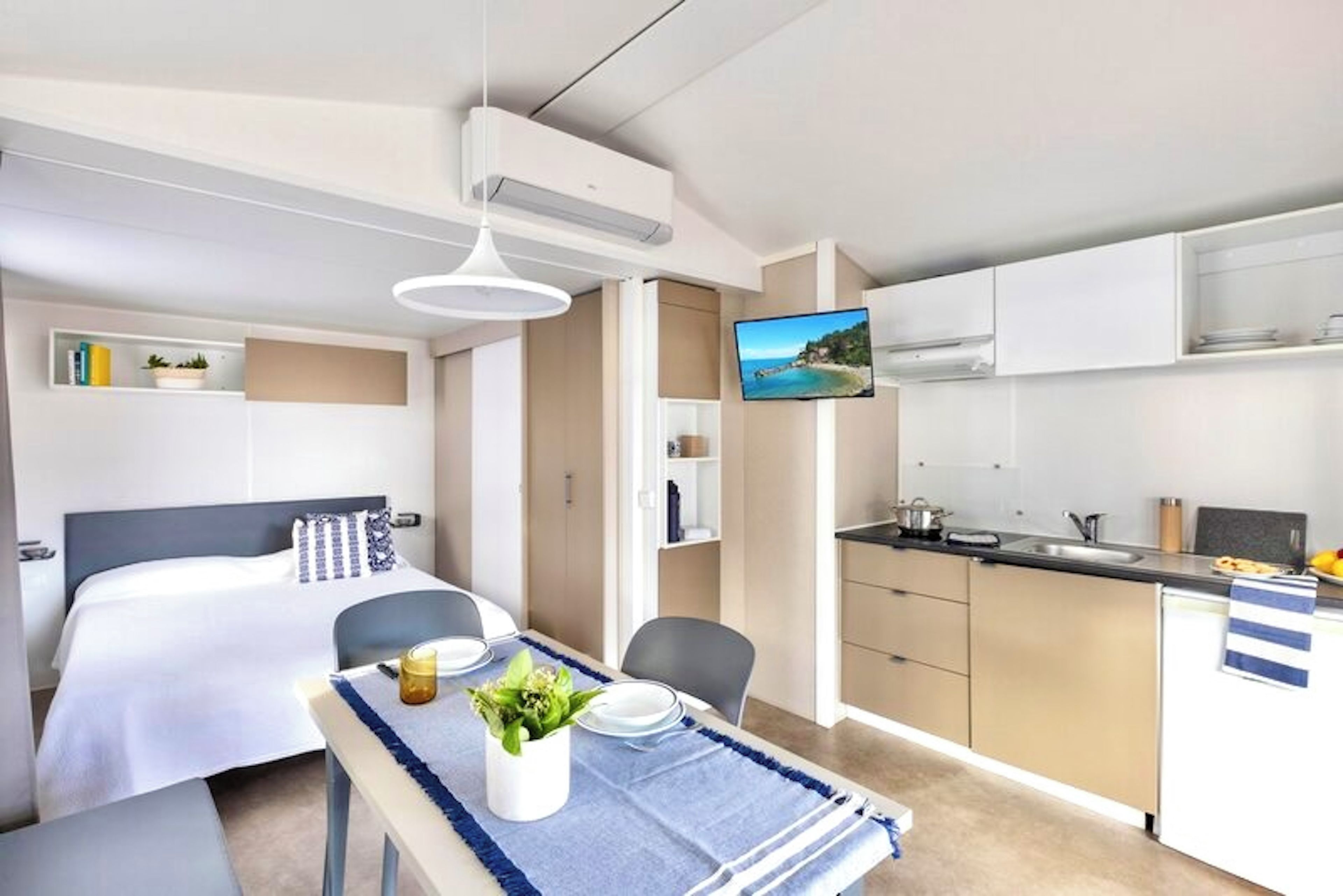 Una habitación de hotel moderna con una cama, una mesa de comedor, un televisor y una kitchenette.