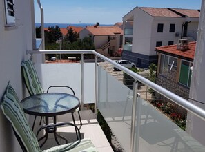 Ein Balkon mit Glastisch und Stühlen, der auf ein Wohngebiet mit Häusern und einem klaren Himmel blickt.