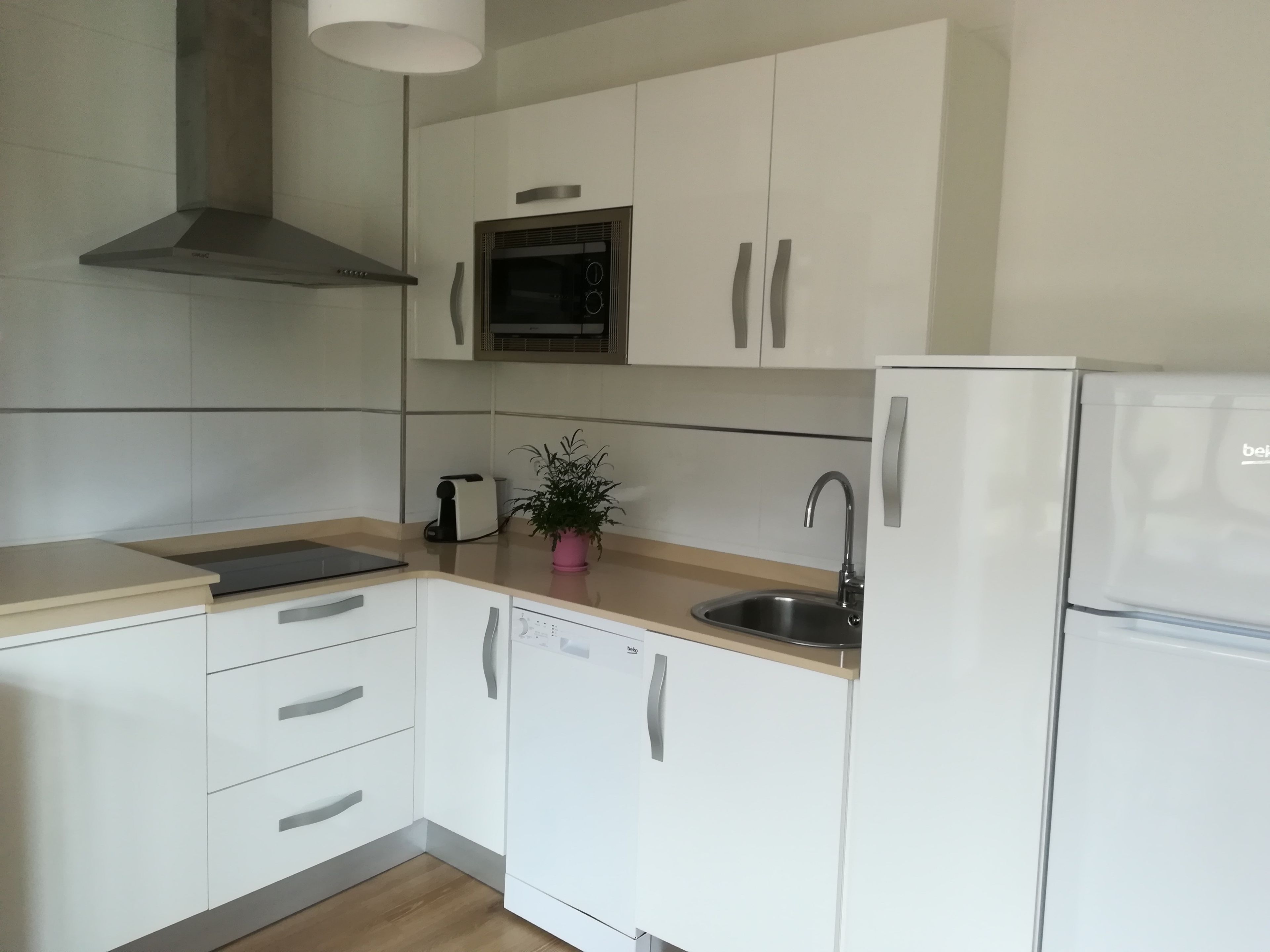 Een moderne keuken met witte kasten, een roestvrijstalen spoelbak, een magnetron en een ingebouwde oven.