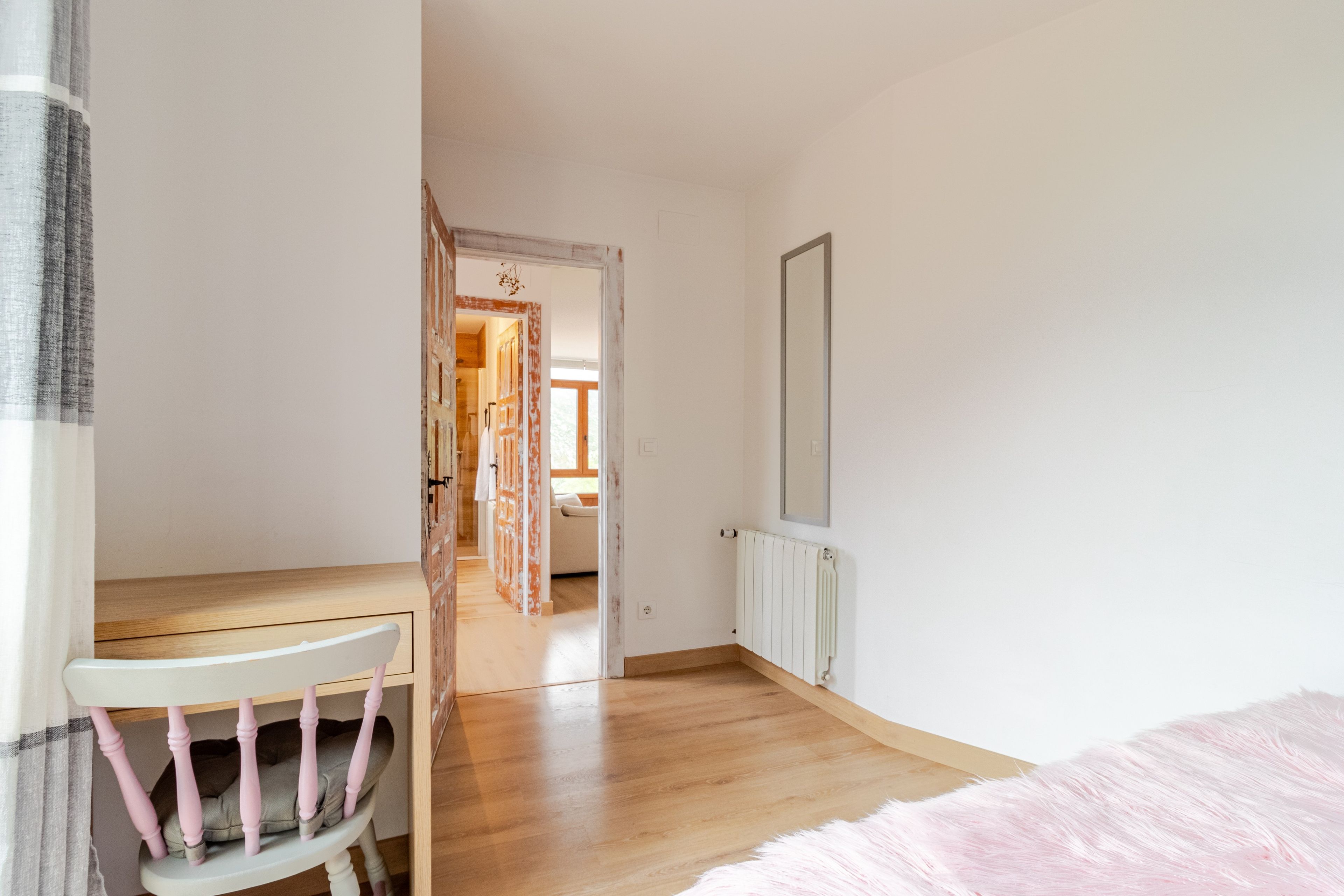 Una habitación con piso de madera, un radiador blanco y una puerta que da a otra habitación.
