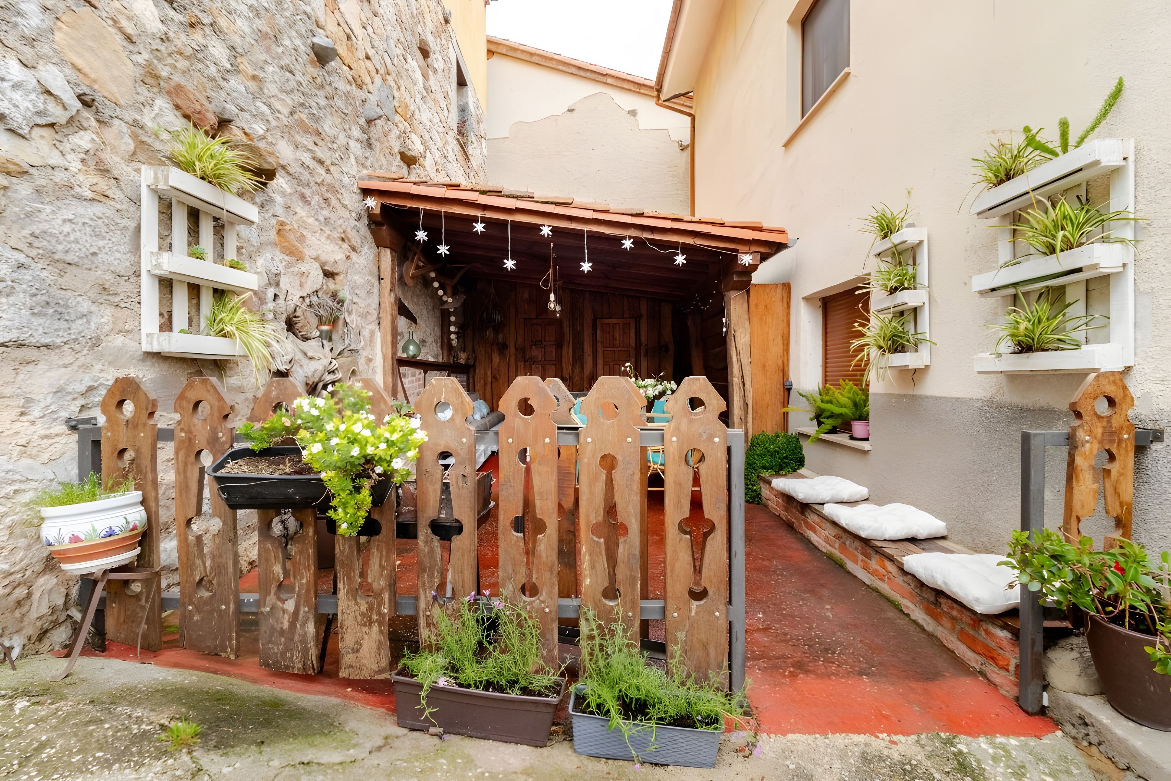 Een landelijke binnenplaats met een houten poort, potplanten en een klein zitgedeelte.