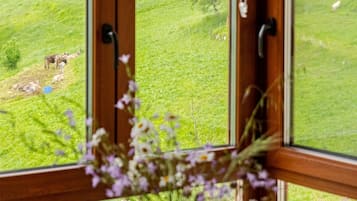 A window with a view of a green landscape, a wooden table with a vase of flowers, and a wooden door with a handle.