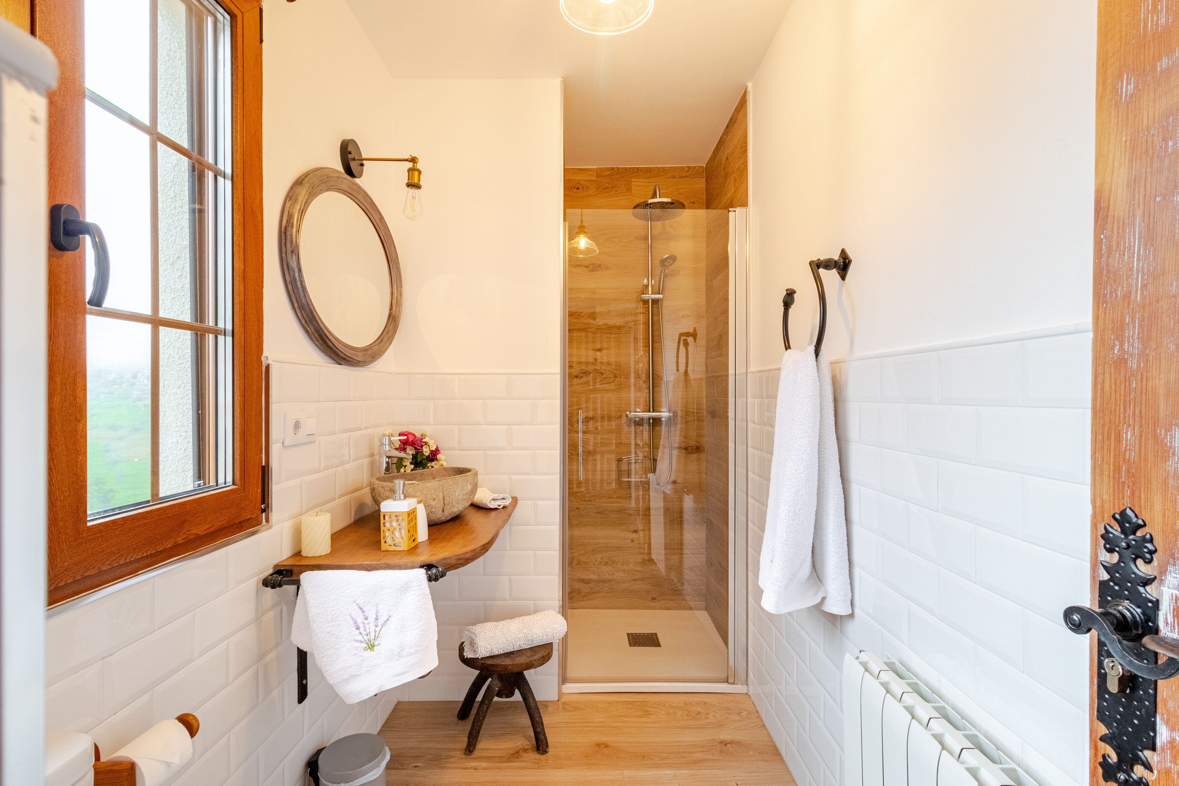 Un baño con tocador de madera, espejo, toallero y zona de ducha.