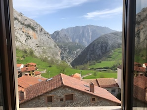 A view of a valley with mountains in the background, a stone building with a red-tiled roof, and a clear sky.