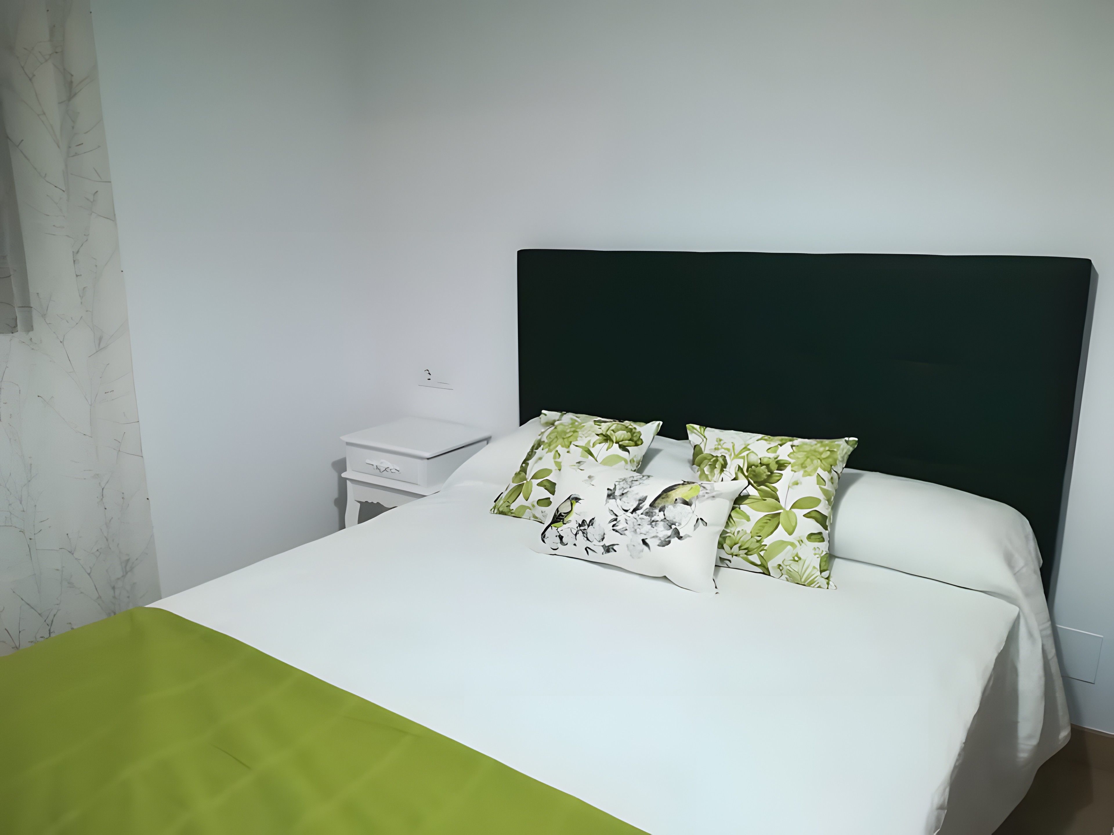 A bed with a white and green bedspread, two pillows with a floral pattern, and a dark headboard.