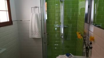 Een badkamer met een douche met glazen wand, een witte wastafel en een handdoekrek met een witte handdoek.