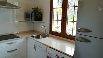Een compacte keuken met een vaatwasser, een ingebouwde magnetron en een raam met uitzicht op een woonwijk.