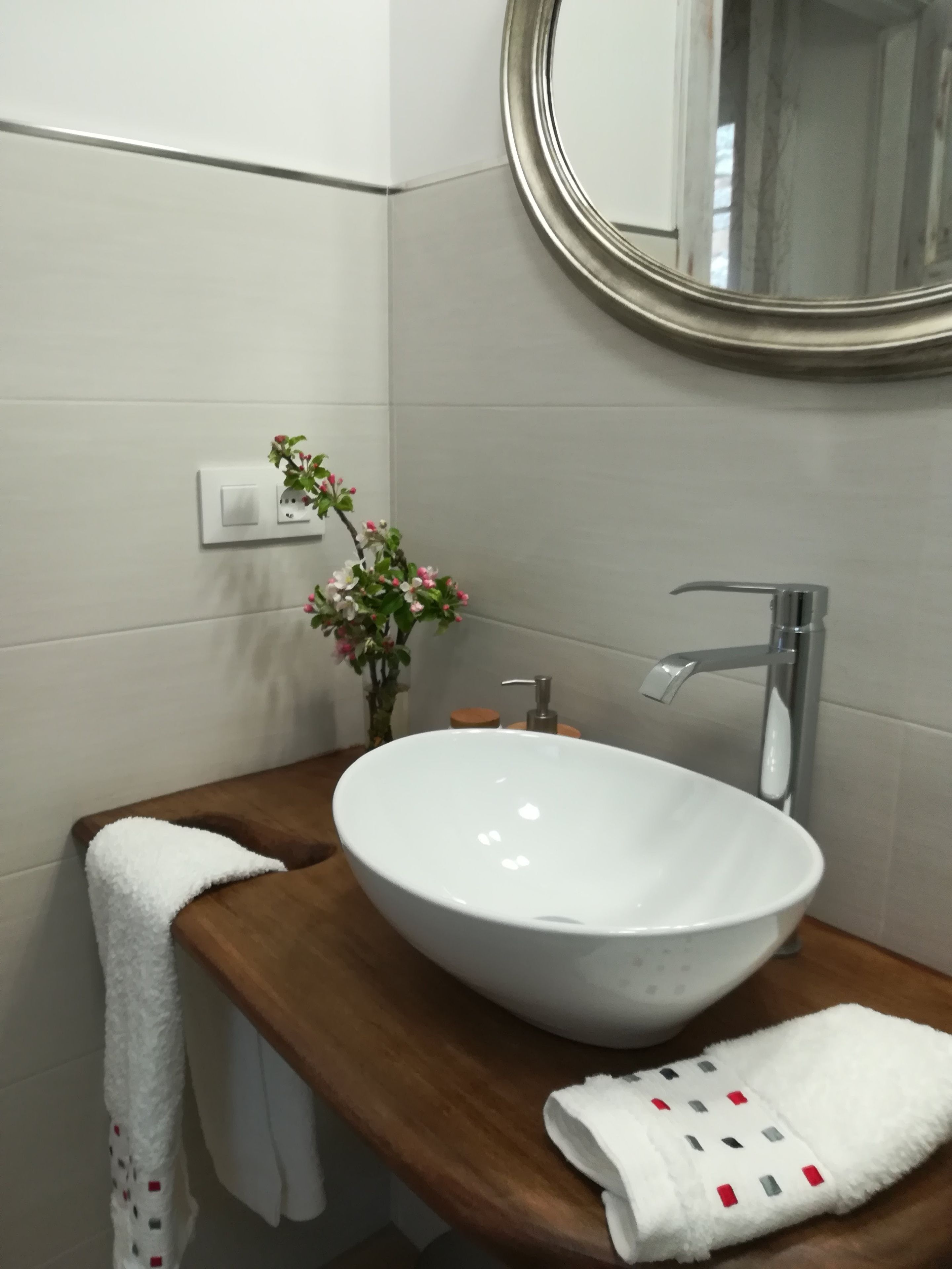 A bathroom with a white sink, wooden countertop, and a round mirror.