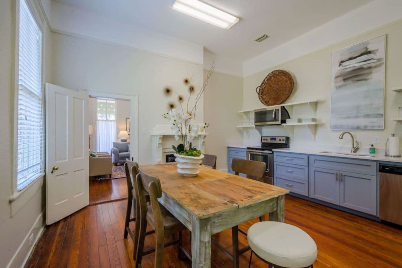 A kitchen with a wooden table, chairs, a vase of flowers, and modern appliances.