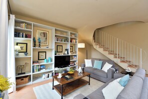 Een woonkamer met een bank, salontafel, boekenkast en een trap.