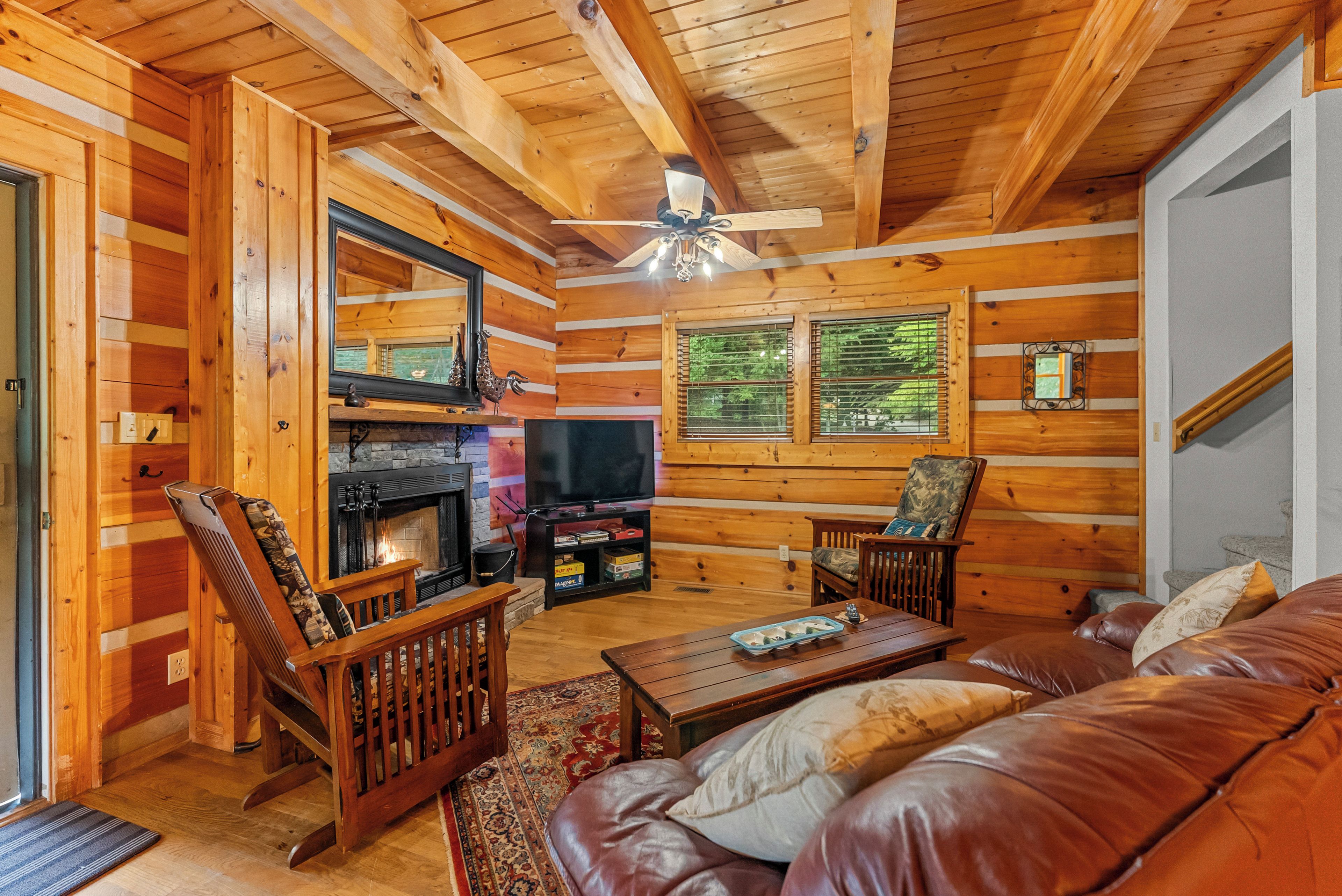 L’intérieur d’une cabane en rondins, avec une cheminée, un téléviseur, un canapé en cuir et un plancher en bois.