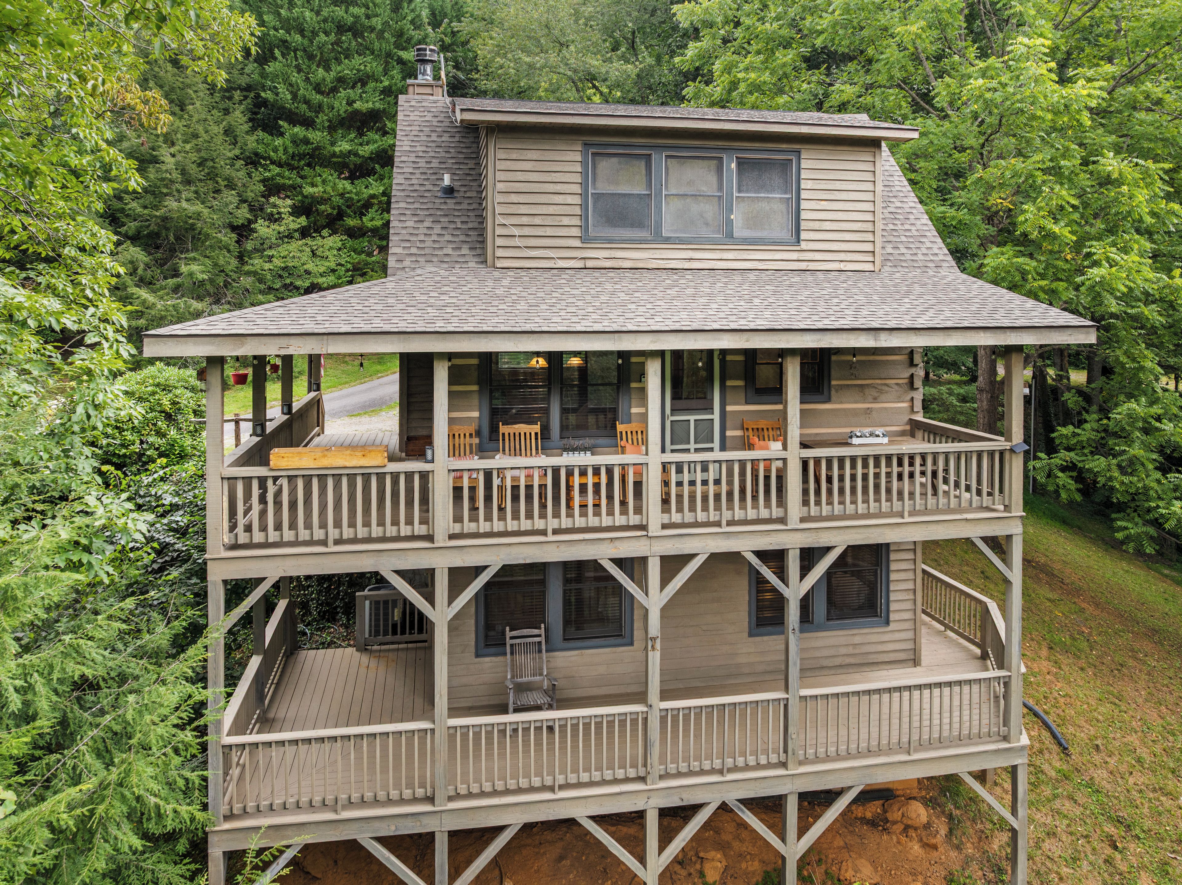 Une cabane en bois à deux étages, dotée d’un balcon et entourée d’une forêt dense.