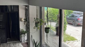 Een modern interieur met een glazen deur naar een balkon, potplanten en een uitzicht op een geparkeerde auto.