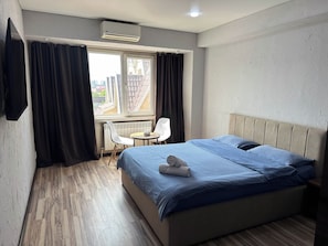 Habitación de hotel con cama, una mesita, dos sillas, ventana con cortinas y un equipo de aire acondicionado.