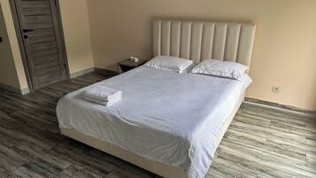 A neatly made bed with a folded white towel, a bedside table with a lamp, and a wooden door.