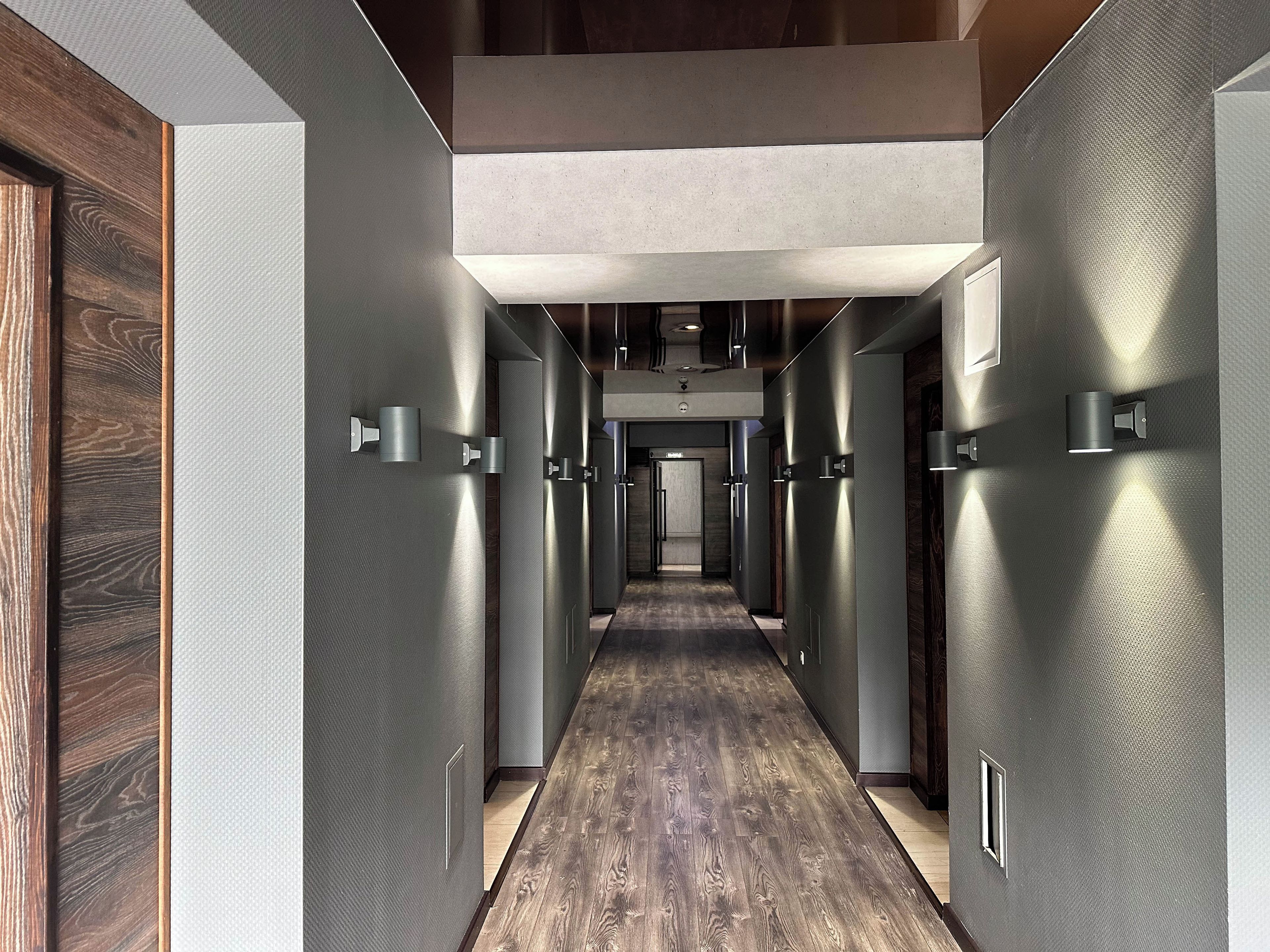 Un pasillo moderno con suelo de madera, paredes metálicas e iluminación empotrada.