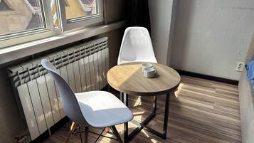 A room with a radiator, a round wooden table, two chairs, and a window with a view of buildings.