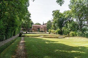 A well-maintained garden with a stone building, neatly trimmed hedges, and a gravel path leading to the entrance. - Charming Vacation Rental at the Foot of Cas Castle - Le Romantique (Espinas)