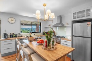 Une cuisine moderne dotée d’un îlot central, d’appareils électroménagers en acier inoxydable et offrant une vue sur l’extérieur.