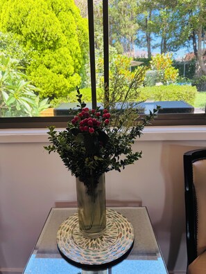 Une plante en pot, ornée de fleurs rouges, est posée sur une table près d’une fenêtre.