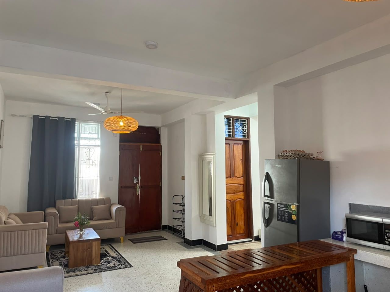 Una sala de estar con un sofá, una mesa de centro y una mesa de comedor con sillas. Hay un refrigerador y un microondas en la zona de la cocina.