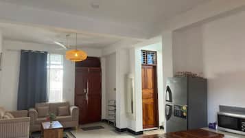 Una sala de estar con un sofá, una mesa de centro y una mesa de comedor con sillas. Hay un refrigerador y un microondas en la zona de la cocina.