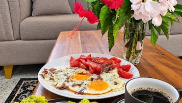 Un desayuno con huevos, tostadas con guacamole, una taza de café y un jarrón con flores.