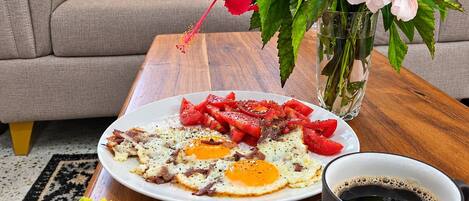 A breakfast setting with a plate of eggs, toast with guacamole, a cup of coffee, and a vase with flowers.