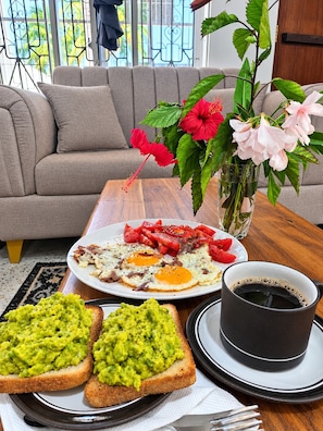 Esmorzar amb un plat d'ous, torrades amb guacamole, una tassa de cafè i un ram de flors.