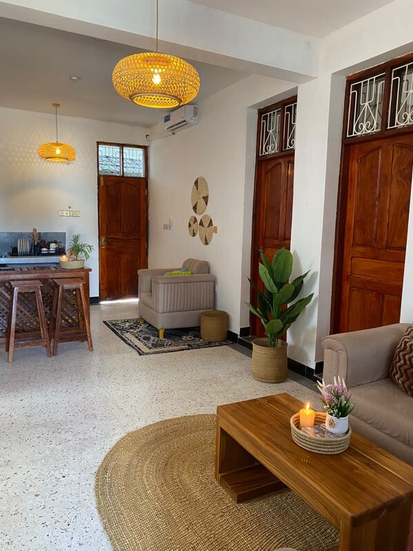 A living room with a sofa, a coffee table, a dining area with chairs, and a kitchen in the background.