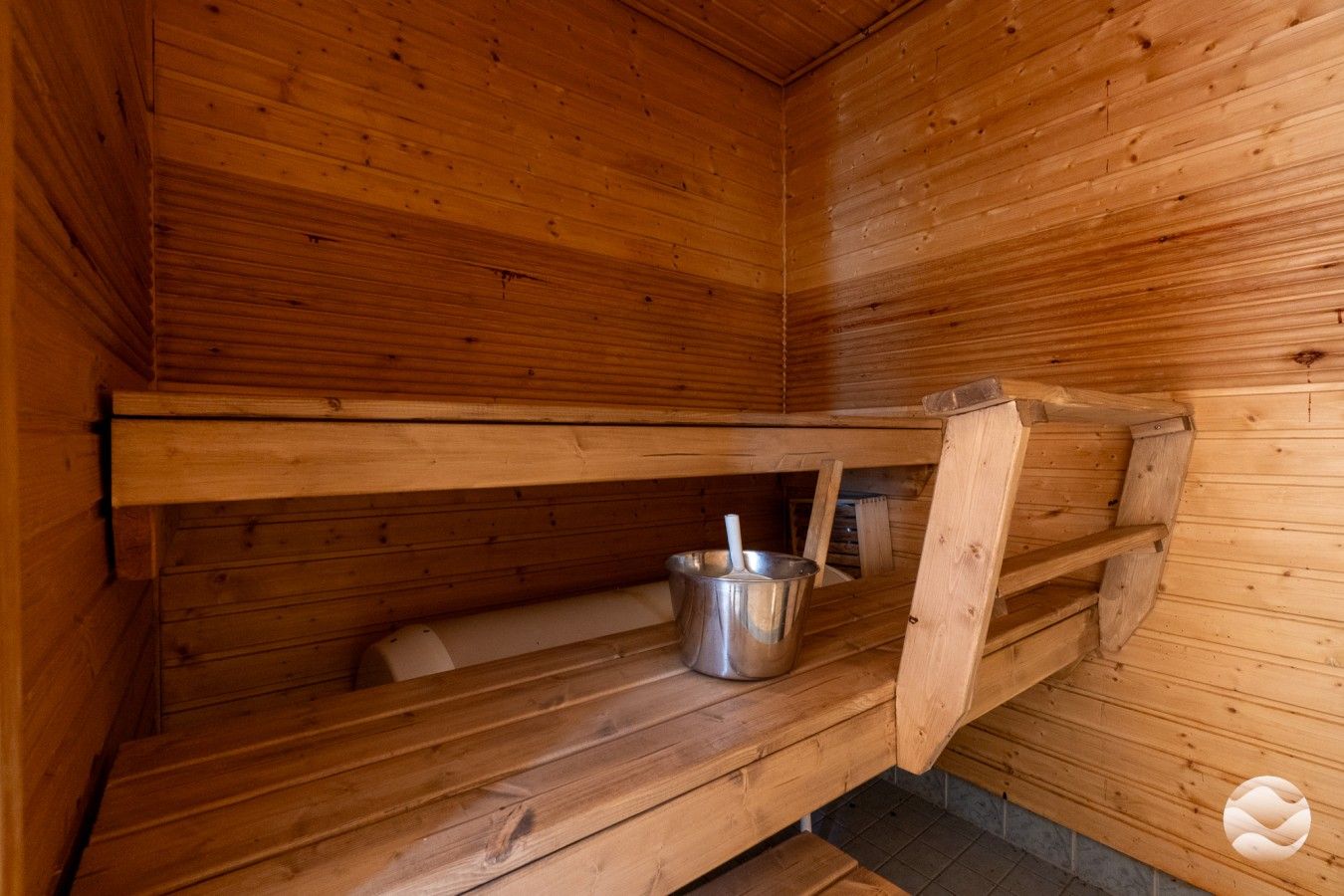 Uma sauna de madeira com bancos e um balde de metal.
