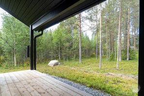 Une terrasse en bois qui mène à un espace abrité d’où l’on peut admirer la vue sur une forêt.