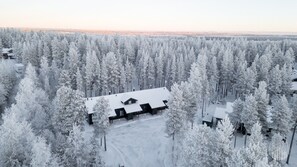 Une forêt enneigée avec une cabane et un bâtiment doté d’un toit en pente.