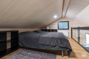 Ein Schlafzimmer mit schrägem Dach, einem Bett mit dunkler Decke, einem Heizkörper und einem Fenster mit Jalousien.