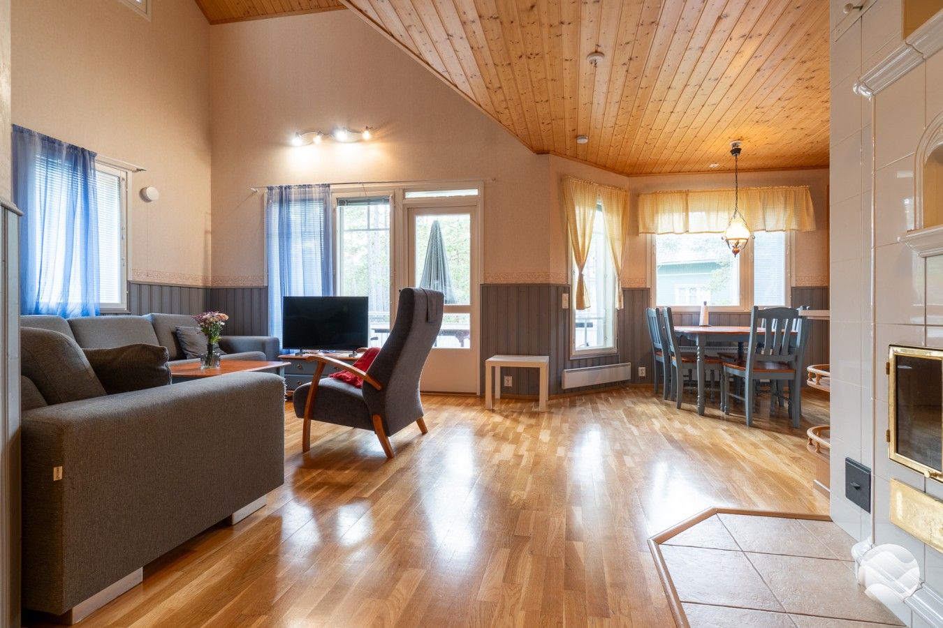 Un vaste espace de vie doté d’un plafond en bois, d’un canapé, d’un téléviseur et d’une table à manger avec des chaises.