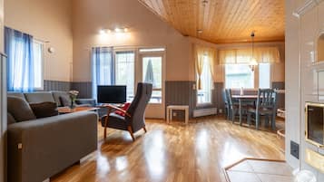 Un vaste espace de vie doté d’un plafond en bois, d’un canapé, d’un téléviseur et d’une table à manger avec des chaises.