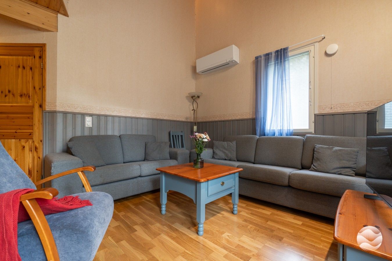 A cozy living room with a wooden ceiling, a grey sofa set, a wooden coffee table, and a blue armchair.