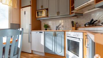 Eine kleine Küche mit Kühlschrank, Mikrowelle, Backofen und Spüle mit Wasserhahn.