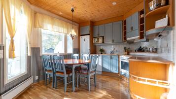 Una cocina con armarios de madera, una mesa de comedor con sillas y un ventanal con cortinas.