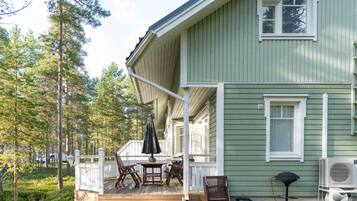 Ein grünes Haus mit Veranda, Gartenmöbeln und Grill.