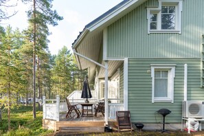 Ein grünes Haus mit Veranda, Gartenmöbeln und Grill.